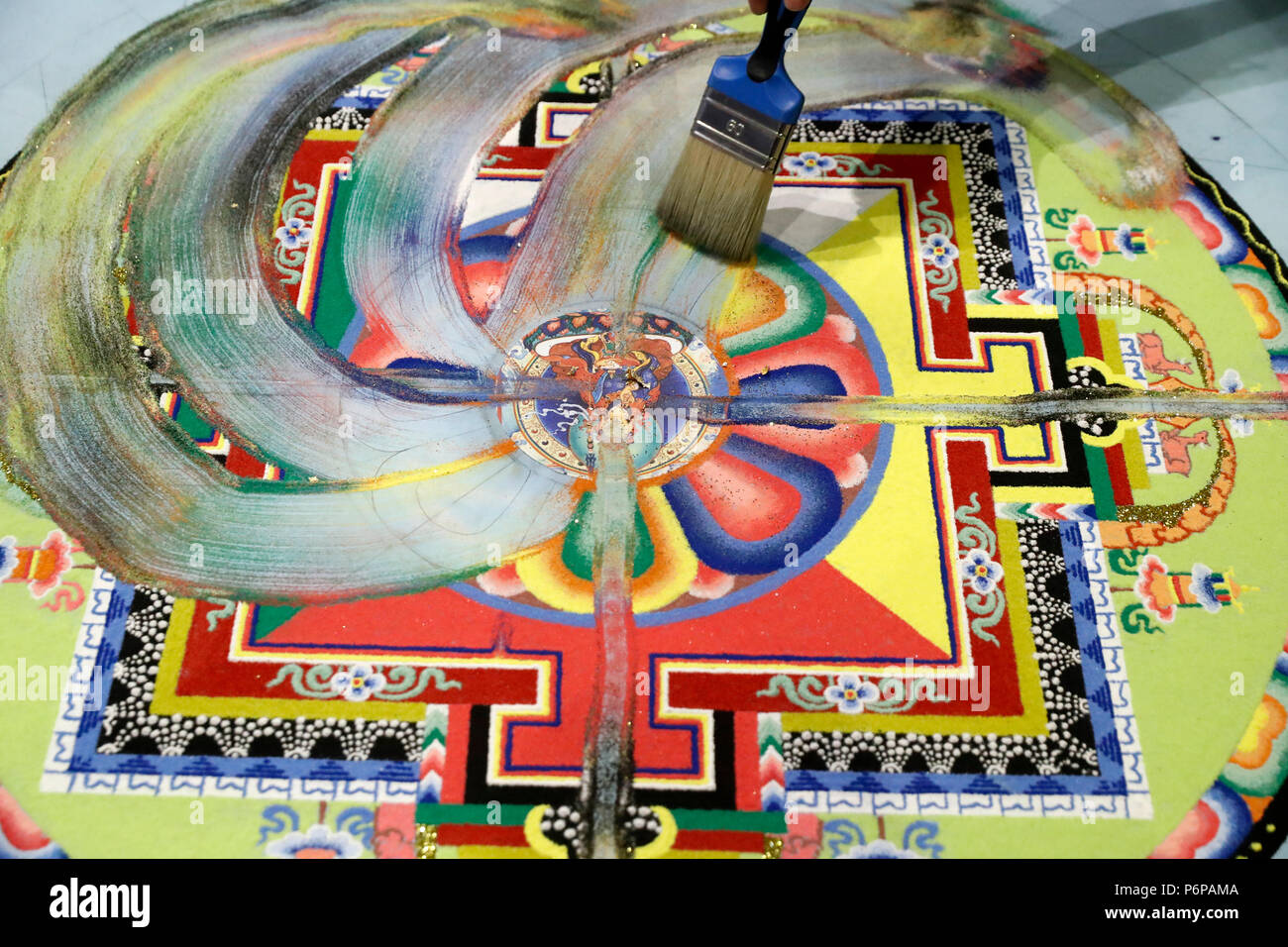 Un moine tibétain utilise un pinceau pour mélanger du sable coloré mandal et balayer dans un tas. Banque D'Images