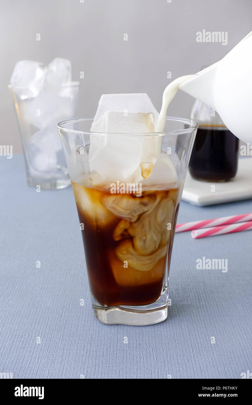 Le lait est versé dans un verre à eau froide préparer du café et des cubes de glace. Banque D'Images