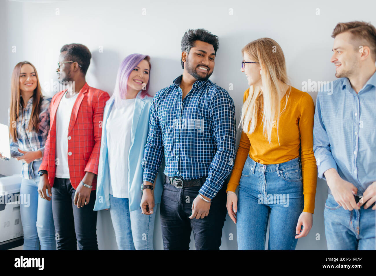 Groupe de personnes se tenant dans la ligne multicolore contre mur blanc. L homme et de la femme vetue de vetements de detente de sourire et de se regarder. Perfomanc Photo Stock