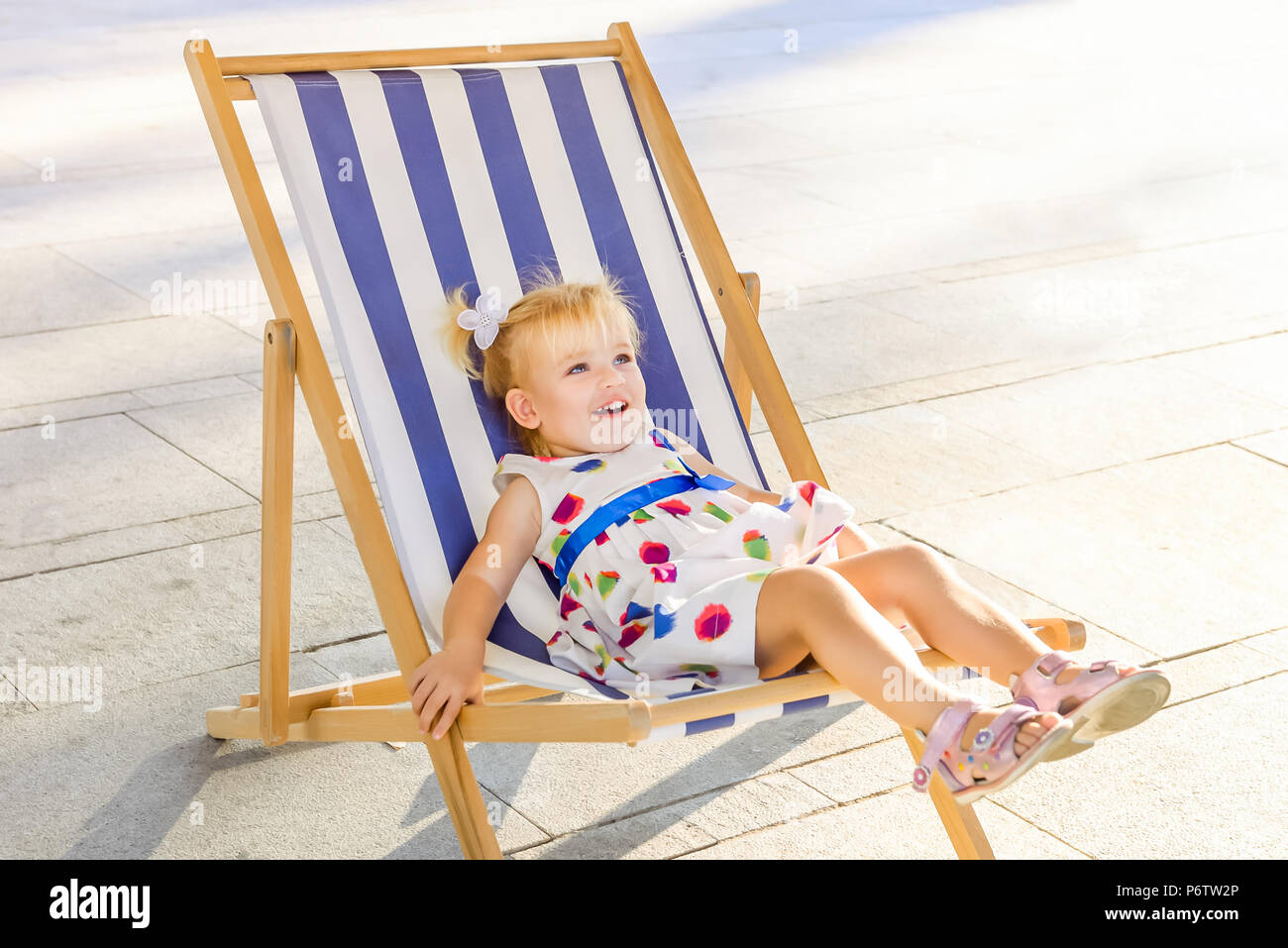 Portrait of smiling adorable bébé fille robe de blondy ou tout-petit enfant  de vous détendre sur un transat ou une chaise longue dans le parc de la  ville zone de loisirs. Selectiv
