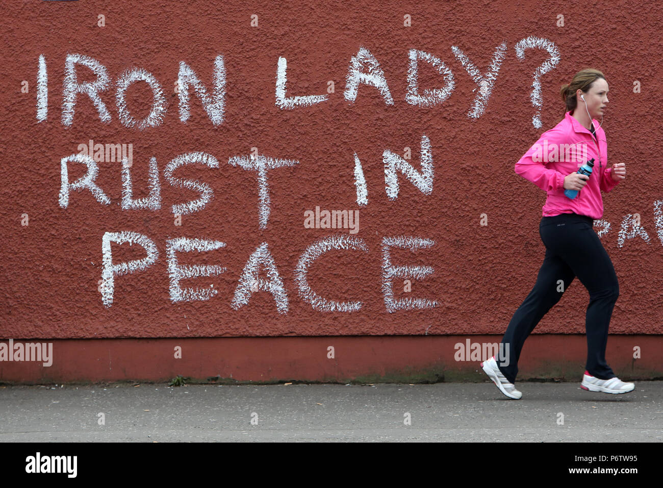 Un jogger passe devant le graffiti qui lit "Dame de fer ? La rouille de la paix" se réfère à l'ancien premier ministre britannique Margaret Thatcher dans l'ouest de Belfast, Irlande du Nord, le 9 avril, 2013 un jour après la mort de Thatcher. La Grande-Bretagne s'est profondément divisé sur l'héritage de l'ancien premier ministre Margaret Thatcher qu'il fait des préparatifs pour le grand enterrement la semaine prochaine de la femme connue dans le monde entier comme la "Dame de fer". Photo/Paul McErlane Banque D'Images