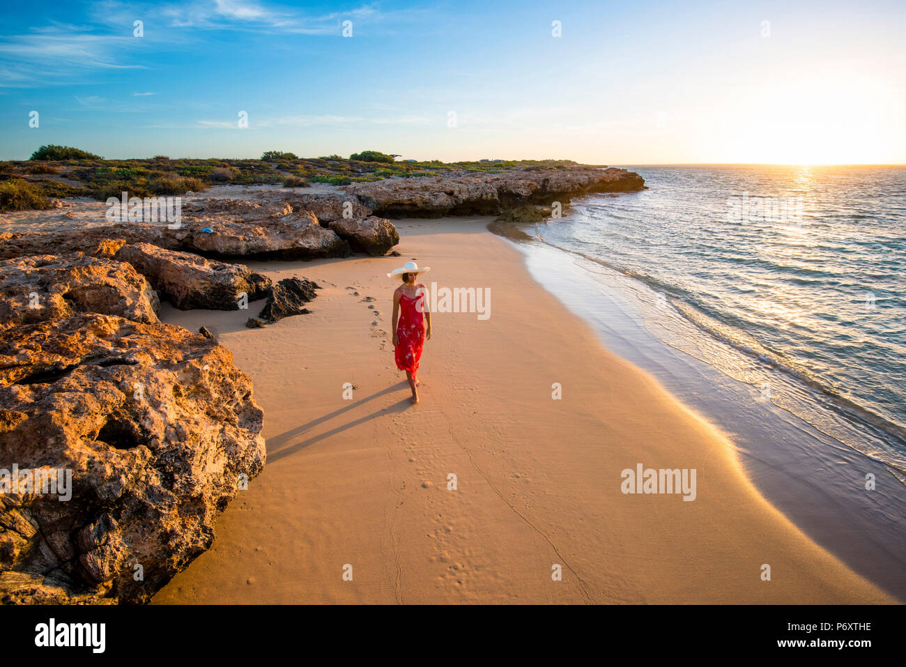Osprey Bay, Cape Range National Park, Exmouth, Australie occidentale, Australie. Femme élégante robe rouge avec chapeau de paille et d'admirer le sunsset (MR). Banque D'Images