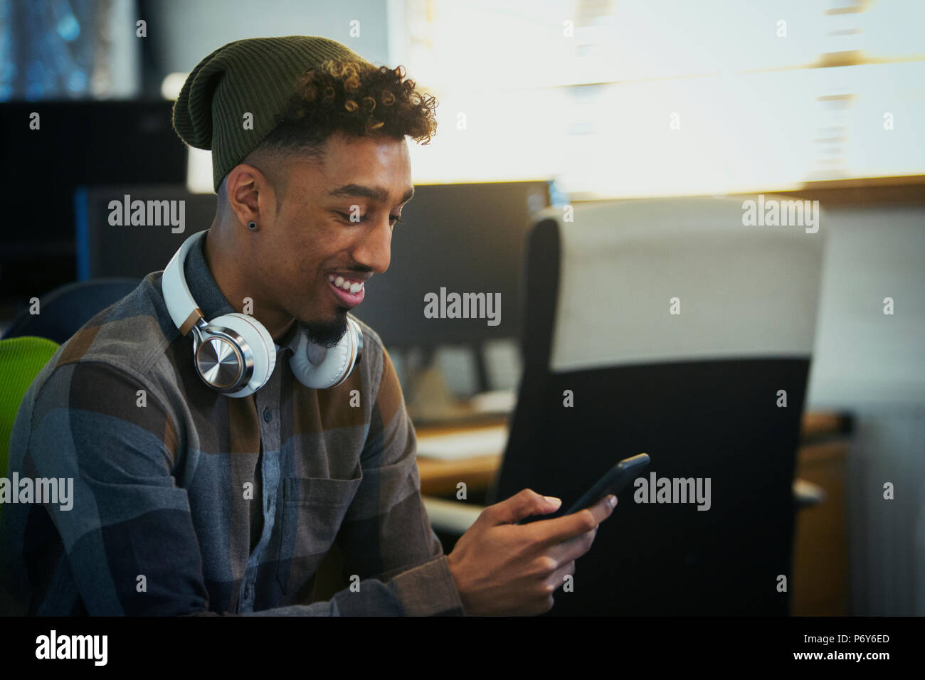 Smiling businessman créative avec des écouteurs à l'aide de smart phone in office Banque D'Images