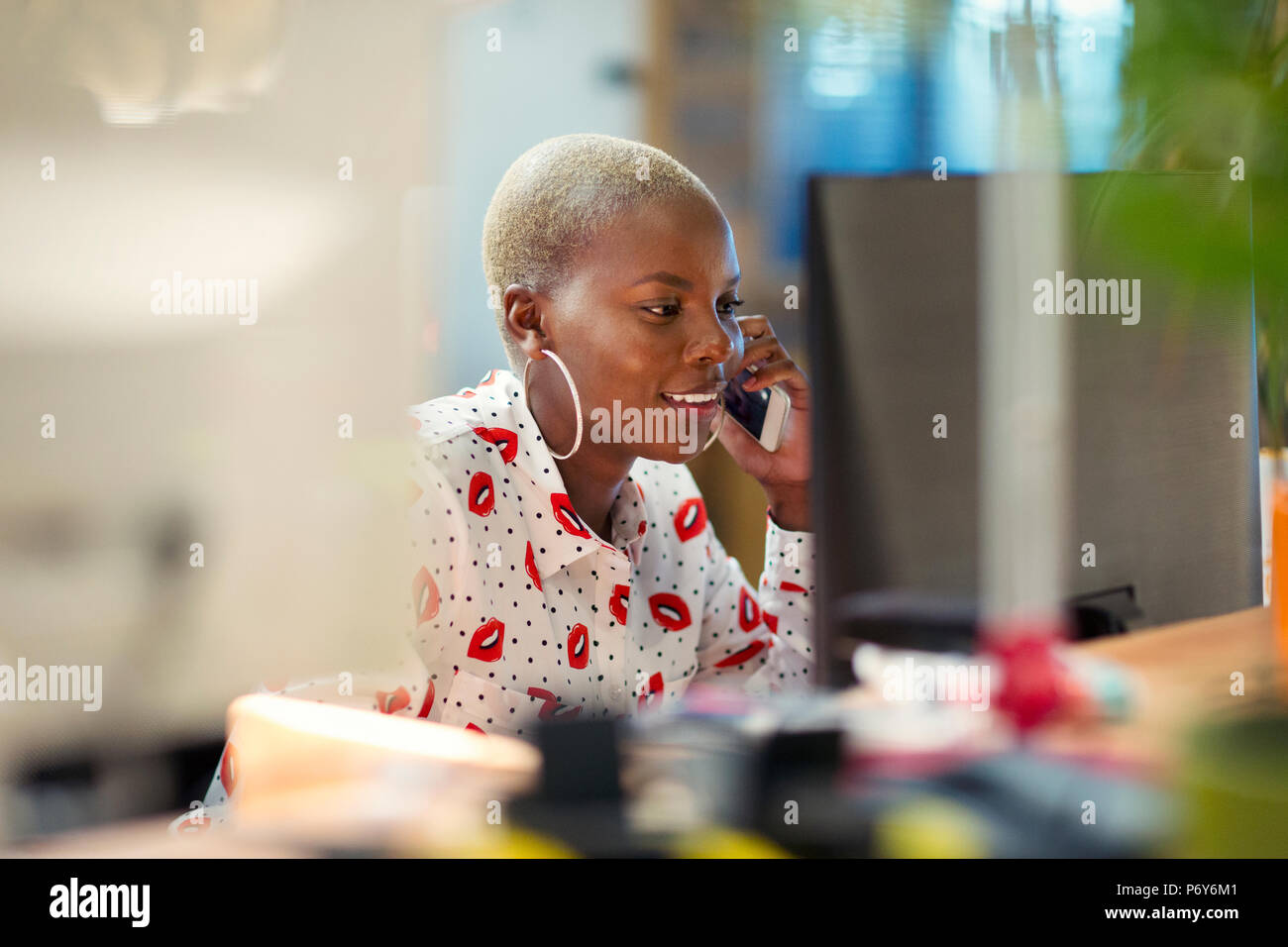 Businesswoman talking on smart phone, travaillant à computer in office Banque D'Images