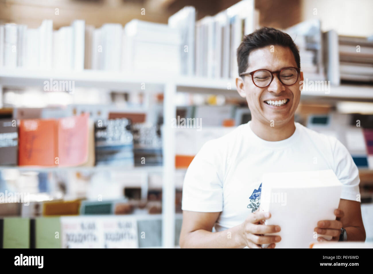 Jeune homme à lunettes heureux holding book avec cache et rire. Banque D'Images