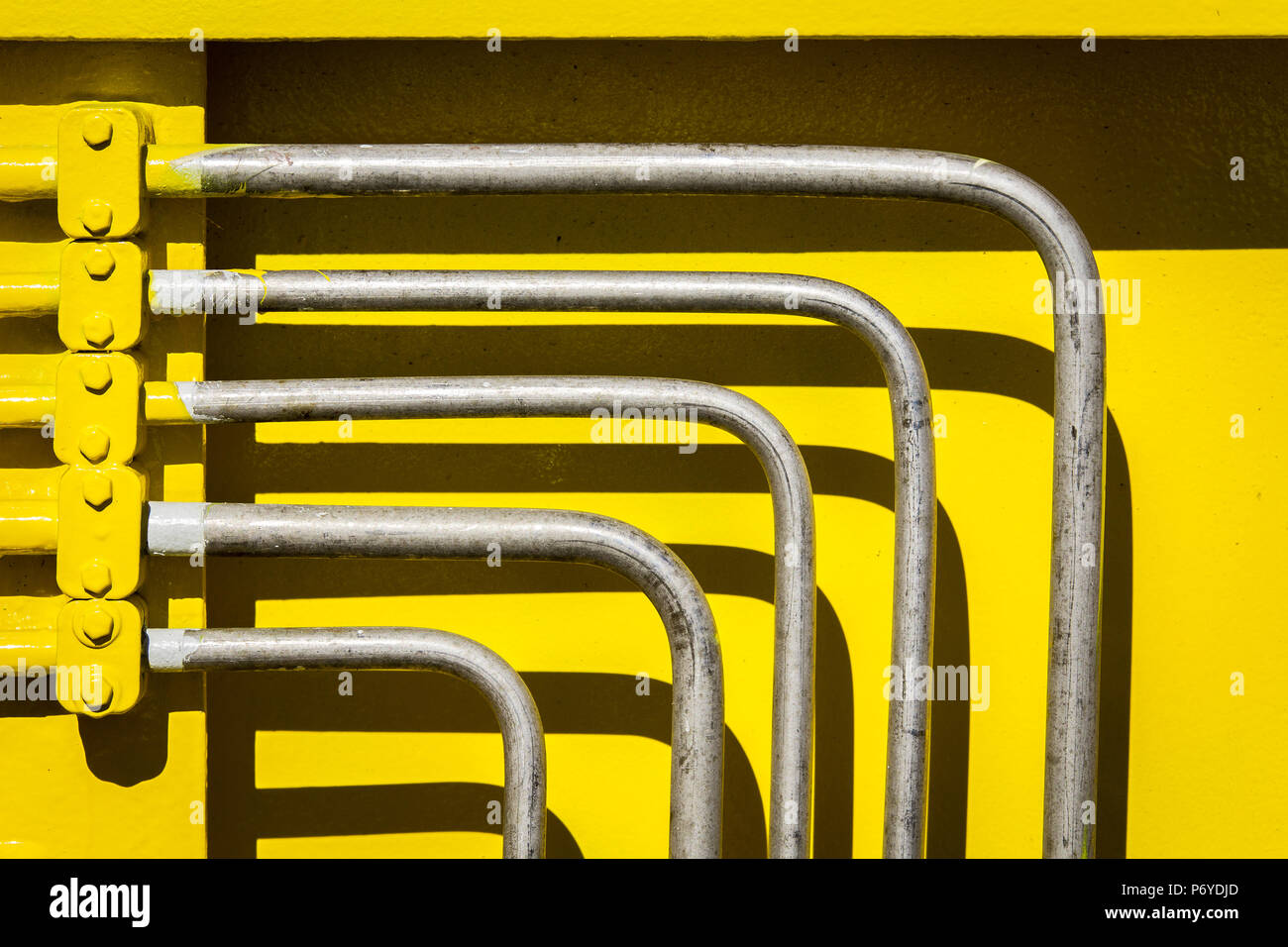 Cinq tuyaux en métal incliné en avant du mur d'acier de couleur jaune vif Banque D'Images