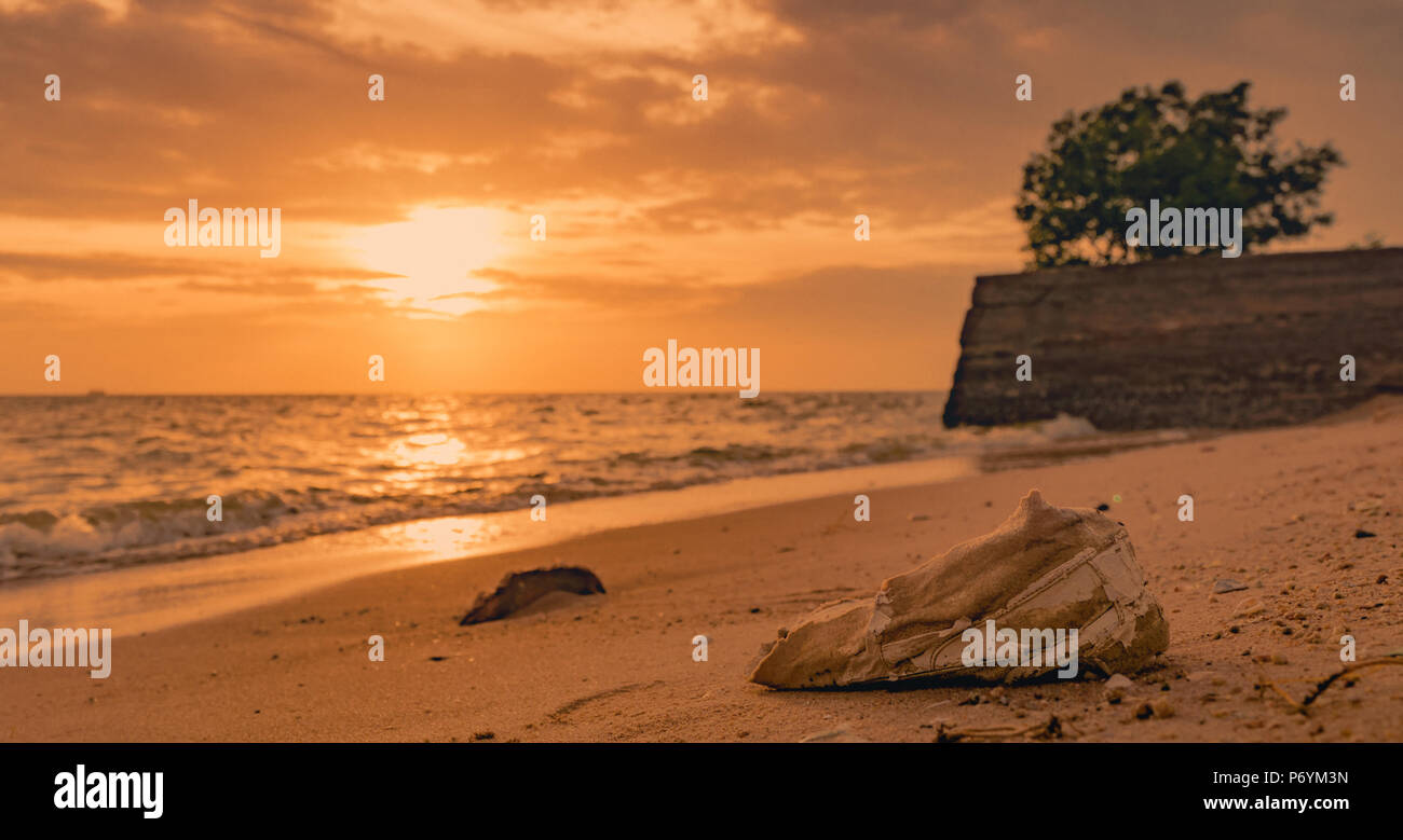 Des ordures sur la plage. La pollution de l'environnement côtier. Problèmes de l'environnement marin. Vieilles chaussures sur le sable plage au coucher du soleil de temps à proximité de la mer. Déchets o Banque D'Images