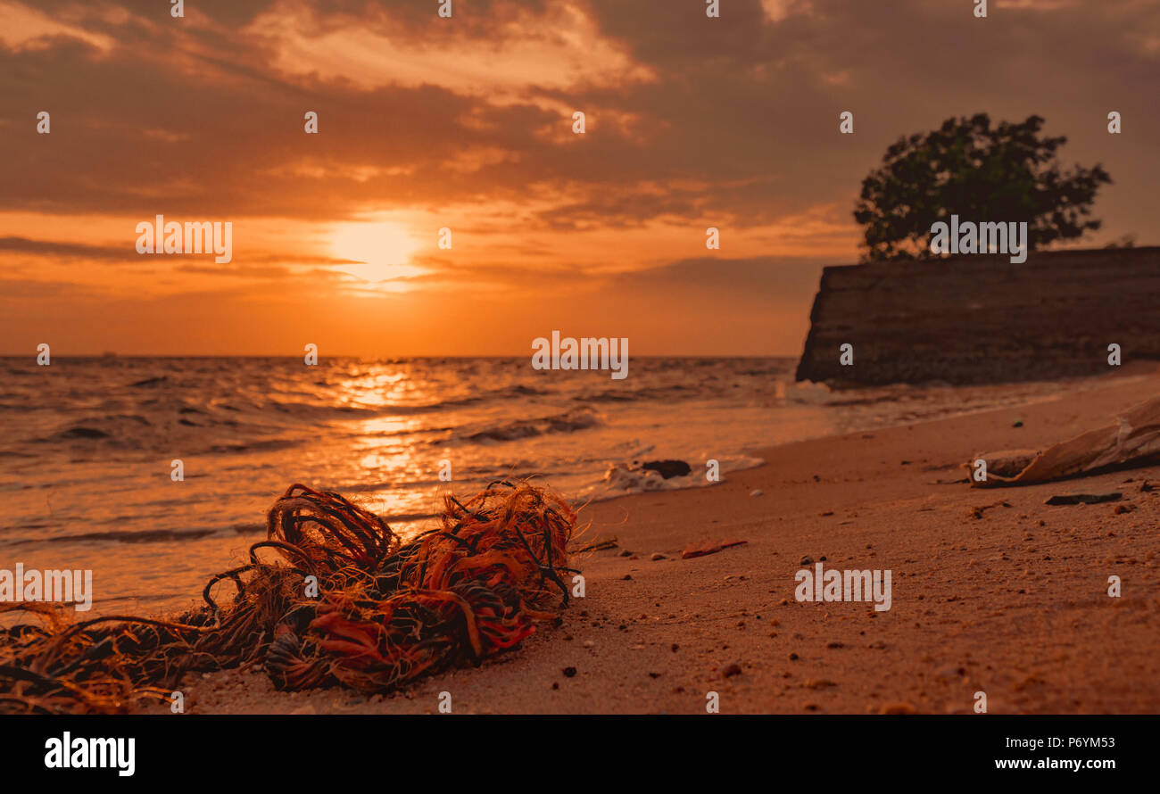 Des ordures sur la plage. La pollution de l'environnement côtier. Problèmes de l'environnement marin. Vieille corde sur plage de sable fin au coucher du soleil près de la mer. Foutaise sur Banque D'Images