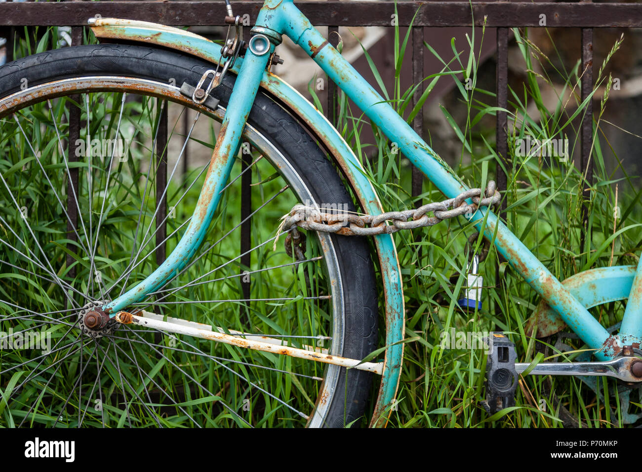 Libre d'une roue avant de vélo avec une chaîne et s'appuyant sur une clôture rouillée. Banque D'Images