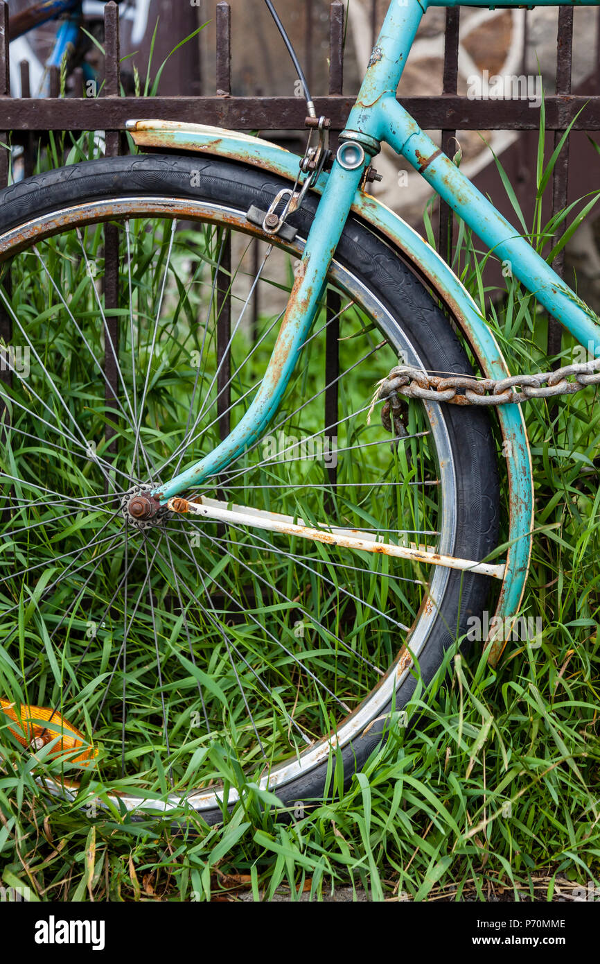 Libre d'une roue avant de vélo avec une chaîne et s'appuyant sur une clôture rouillée. Banque D'Images