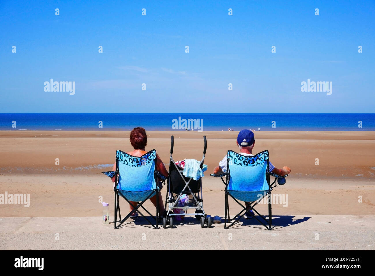 Couple assis dans les mêmes chaises pliantes avec bébé en poussette entre eux sur la plage de Blackpool sur une chaude journée d'été Banque D'Images