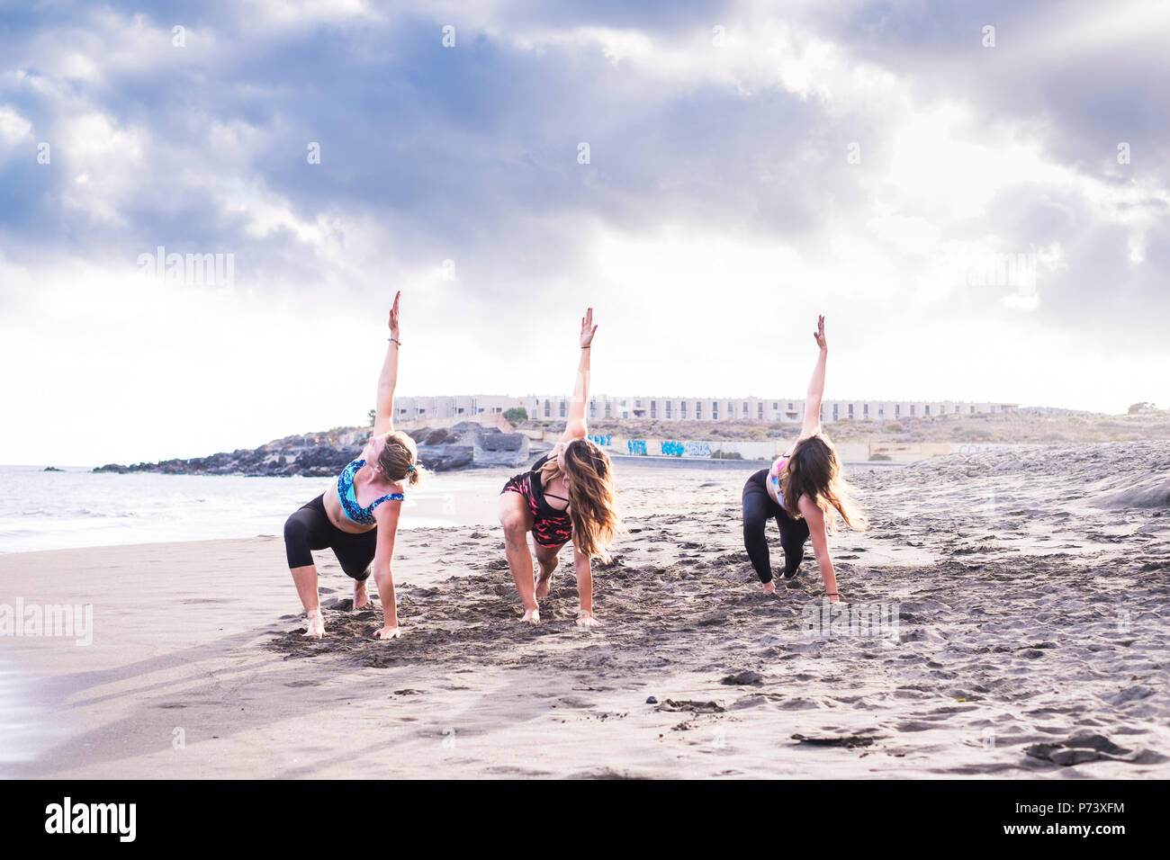 Groupe de trois personnes women friends faire des exercices d'équilibre et de force comme le yoga et pilates sur la plage de sable et de la côte. lieu pittoresque au cours de beauti Banque D'Images