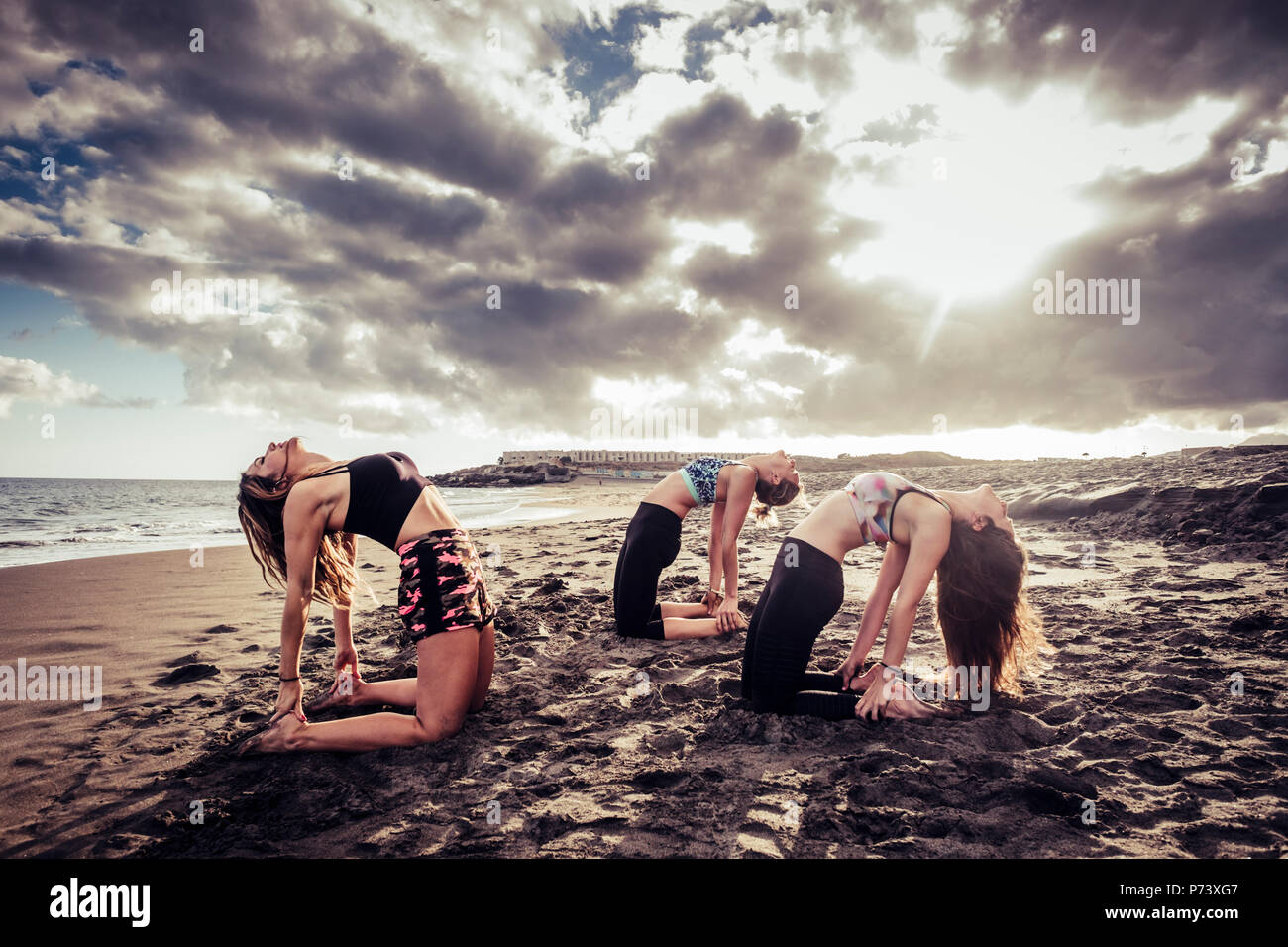 Scenic capture avec trois jeunes beaux modèles chers d'entraînement pilates et yoga à la plage sur le sable. Les nuages et la lumière du soleil au cours des su Banque D'Images