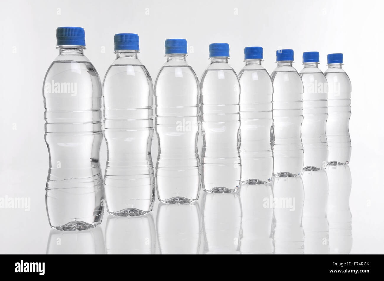 8 bouteilles d'eau en plastique avec couvercles bleu dans une rangée Banque D'Images