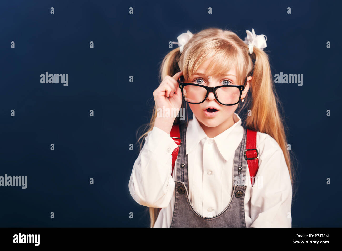 Portrait of a souligné surpris kid girl élève porte lunettes avec sac à dos avant de l'arrière-plan bleu-foncé Banque D'Images