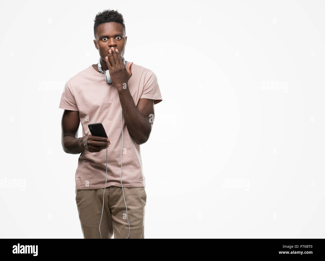 Young african american man wearing headphones holding smartphone et couvrir la bouche à part choqué avec honte pour erreur, expression de la peur, peur Banque D'Images