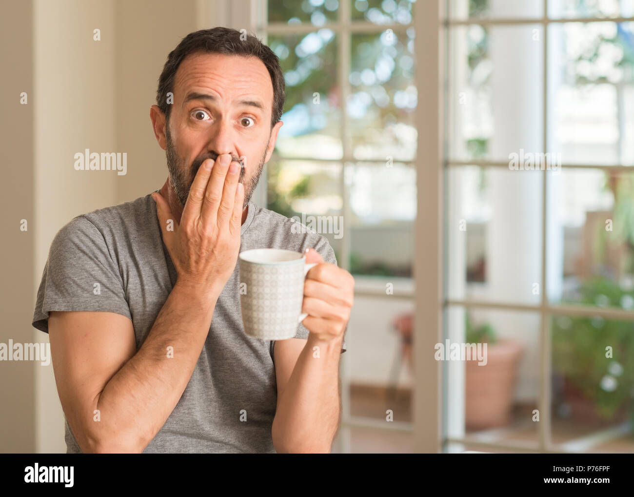 Homme d'âge moyen de boire du café dans une tasse couvrir la bouche à part choqué avec honte pour erreur, expression de la peur, peur en silence, concept secret Banque D'Images