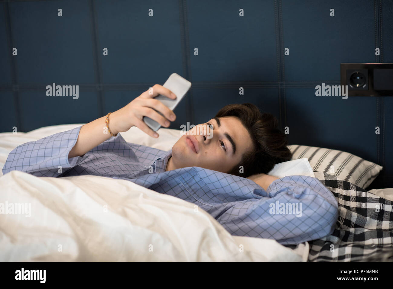 Beau jeune homme au lit en pyjama et en utilisant votre smartphone. Banque D'Images