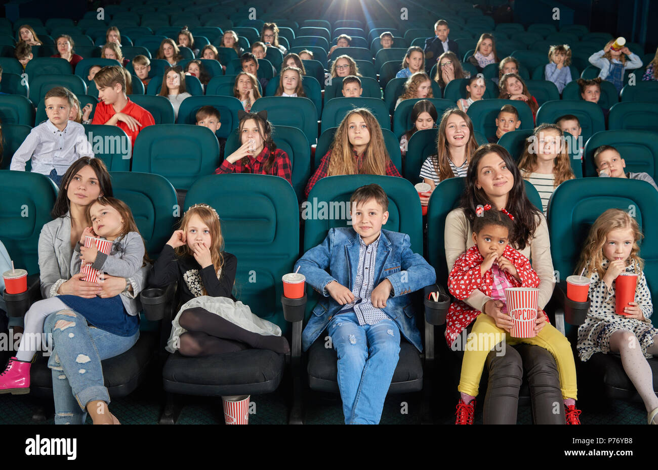 Les jeunes spectateurs assis dans un cinéma et regarder des dessins animés. Les adolescents et les enfants en sirotant des boissons gazeuses et eating popcorn. Jolies filles stit Banque D'Images