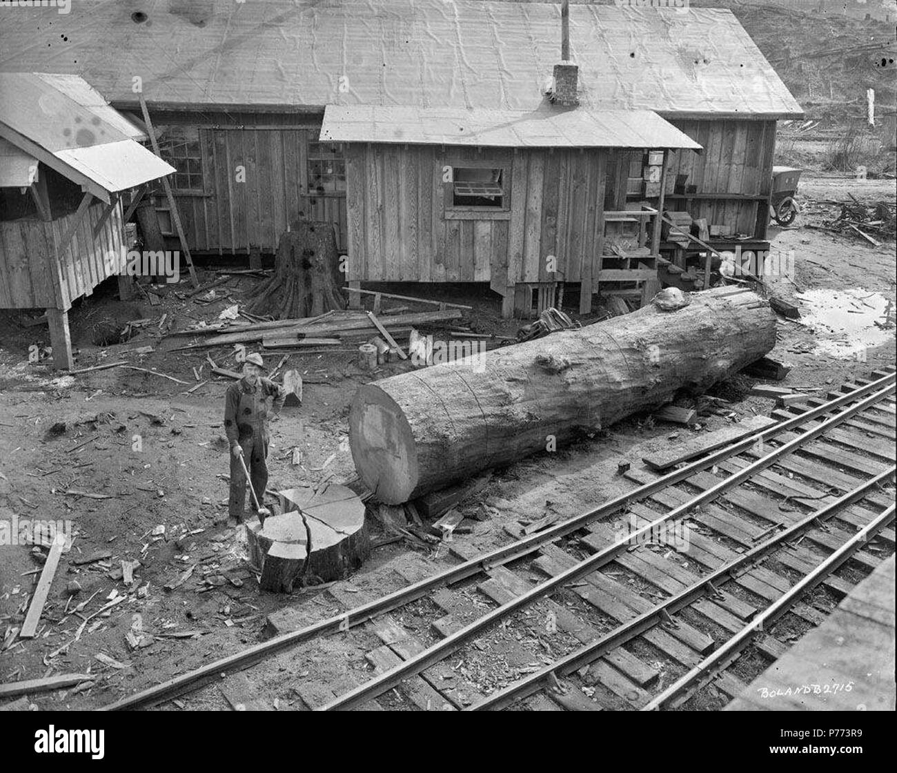 . Petit bois de coupe. Anglais : coupe à l'embrasement de l'enregistreur de journal et Linco Lumber Company à Lindberg, Washington. Le bûcheron, qui tient une hache, se situe à côté de l'embrasement qu'il vient de couper dans un grand journal tronçonne. Dans l'arrière-plan est une maison à ossature bois. 3 mars 1920 7 Journal Linco et petit bois de coupe de bois Banque D'Images