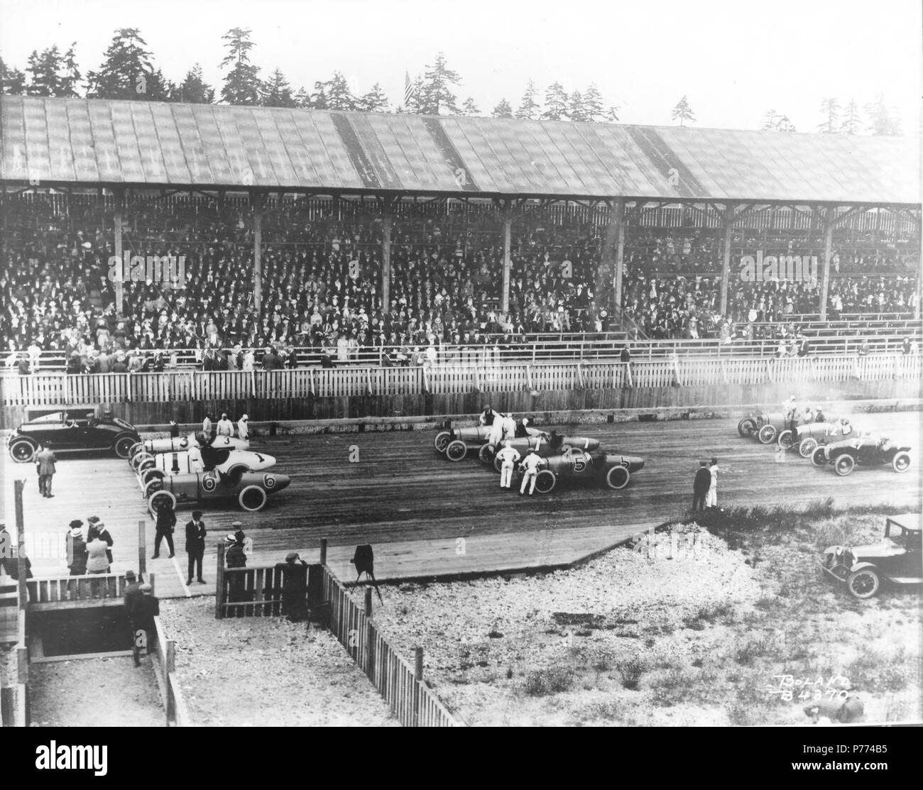 . Marvin D. Collection Boland BOLAND-B4370. Anglais : Vingt mille race fans entassés dans les gradins couverts de la Tacoma Speedway pour regarder le 4 juillet, 1921 Speedway Classic. Les pilotes, les mécaniciens et les officiels de la course sur la piste du conseil avant le début de la course de 250 milles. Les voitures de course sont alignés sur la piste trois au courant, avec la Speedster Marmon pace car dans le plomb. Dans la première rangée sont, de gauche à droite, # 6 Roscoe Sarles' Duesenberg, # 1 Eddie Hearne's Revere et spécial # 3 Frank Elliott Leach spécial. Rangée du milieu : # 5 Joe Thomas Duesenberg, # 7 Eddie Miller, la voiture n°2 pour Banque D'Images