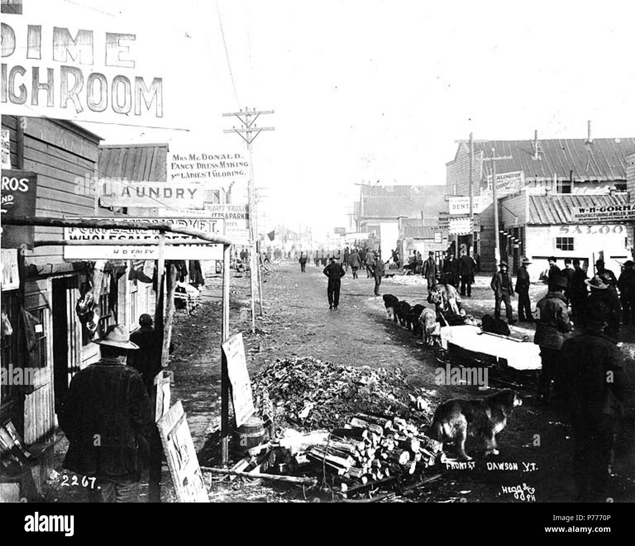 . Anglais : St.avant au cours de l'hiver, Dawson, Territoire du Yukon, ca. 1899. Anglais : Indique les établissements commerciaux et de transport de l'équipe de chien de blocs de glace le long de la rue Front . Légende le droit : 'la rue Front Dawson YUK.' . L'or du Klondike. Sujets (LCTGM) : rues--Yukon--Dawson ; annonces--Yukon--Dawson ; Tailleurs--Yukon--Dawson ; débits de boissons (bars)--Yukon--Dawson ; des quartiers d'affaires--Yukon--Dawson ; chiens de travail--Yukon--Dawson ; Chariots et wagons--Yukon--Sujets Dawson (LCSH) : la rue Front, à Dawson (Yukon) ; Mme McDonald Fancy Dress et Mesdames la couture (Dawson (Yukon) vers 1899 5 . Banque D'Images