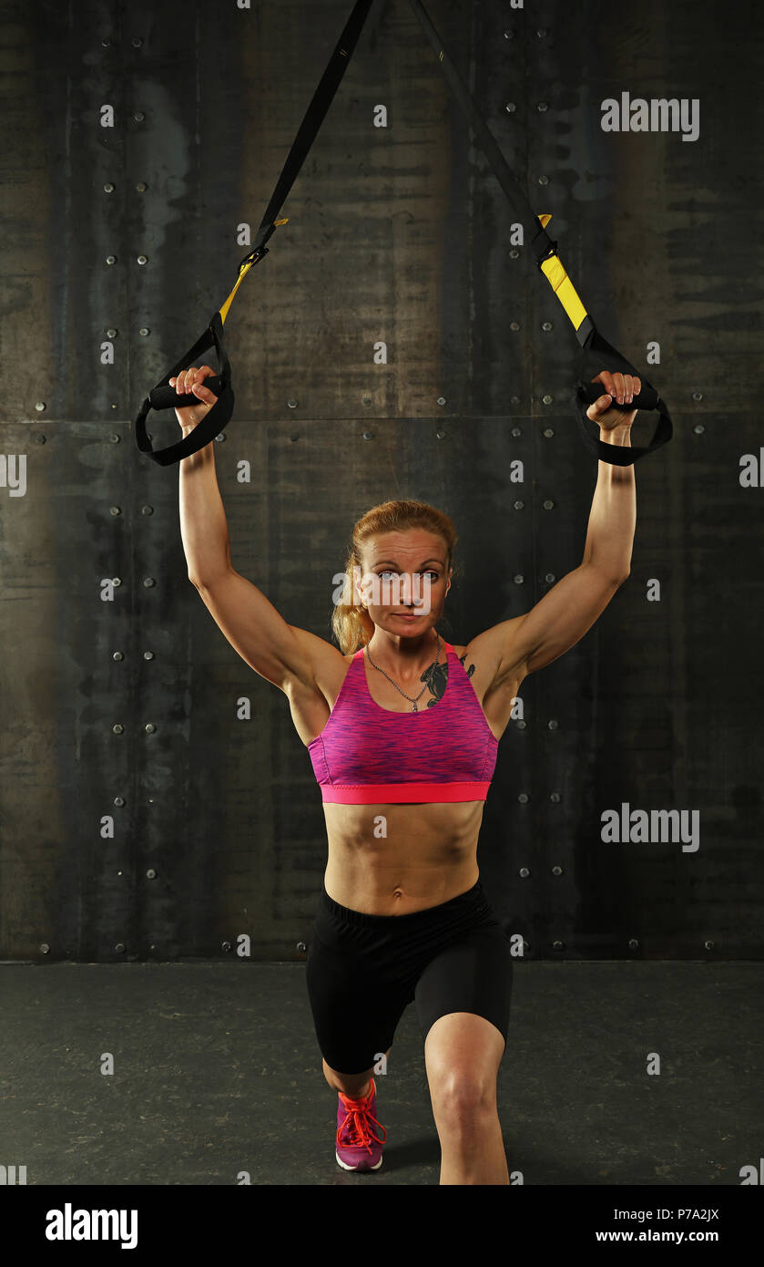 Une jeune femme athlétique au moyen-âge, l'exercice de formation crossfit avec trx suspension sangles de remise en forme sur fond sombre, vue avant, à la recherche en c Banque D'Images