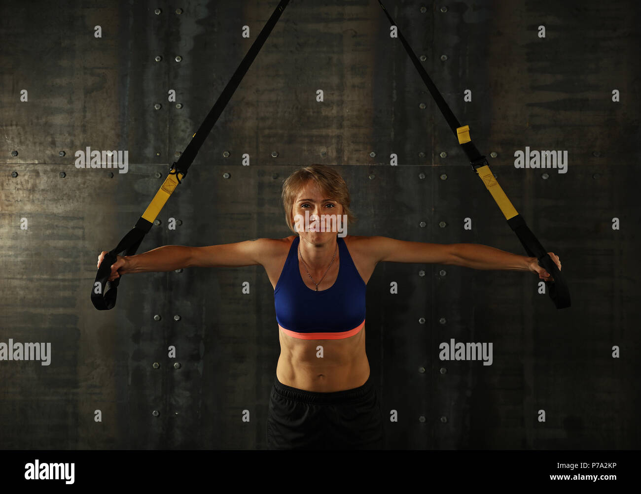Une jeune femme athlétique au moyen-âge, l'exercice de formation crossfit avec trx suspension sangles de remise en forme sur fond sombre, vue avant, à la recherche en c Banque D'Images