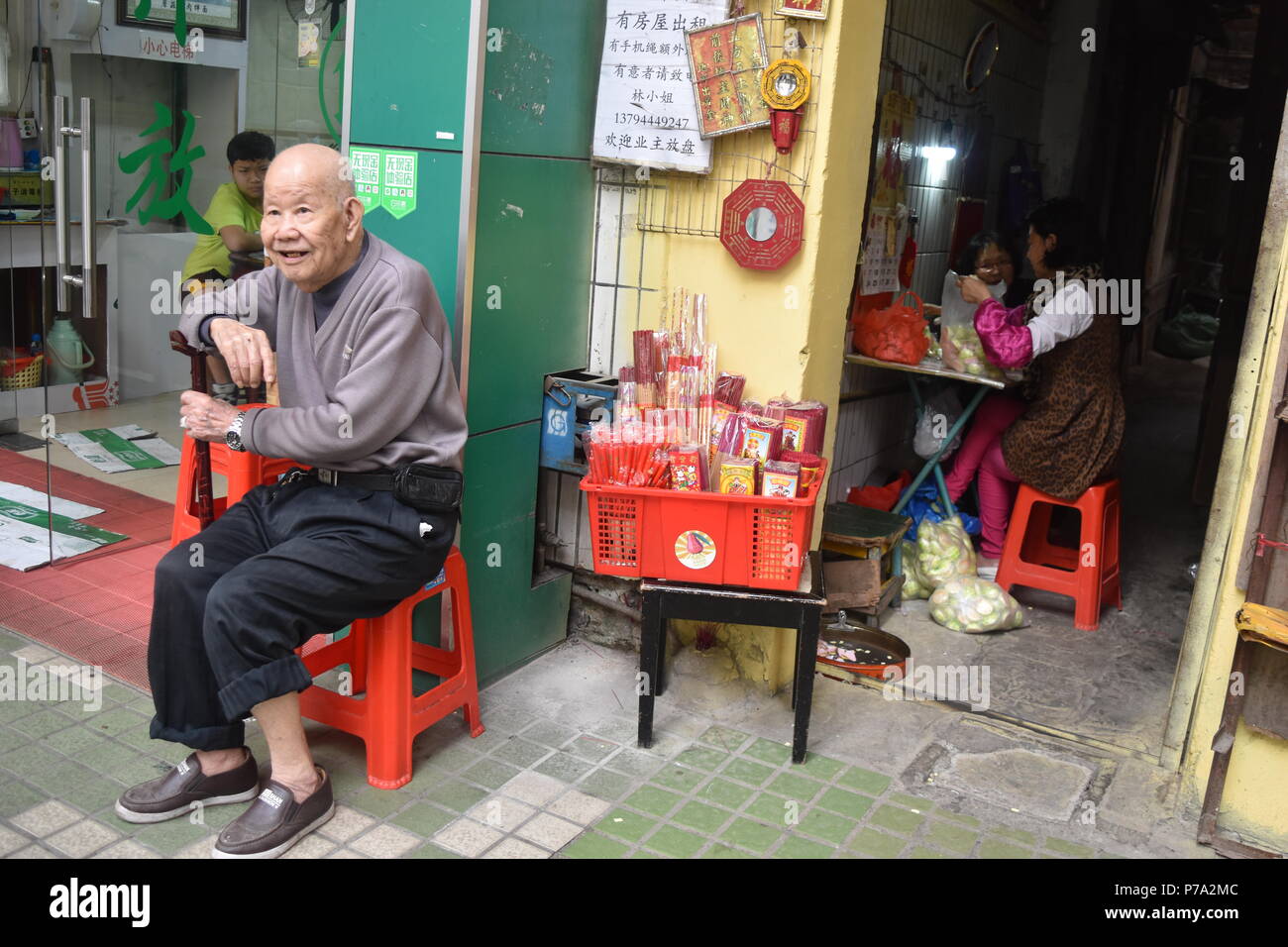 L'homme chinois ancien siège au centre-ville de Guangzhou par un trottoir shopfront Banque D'Images