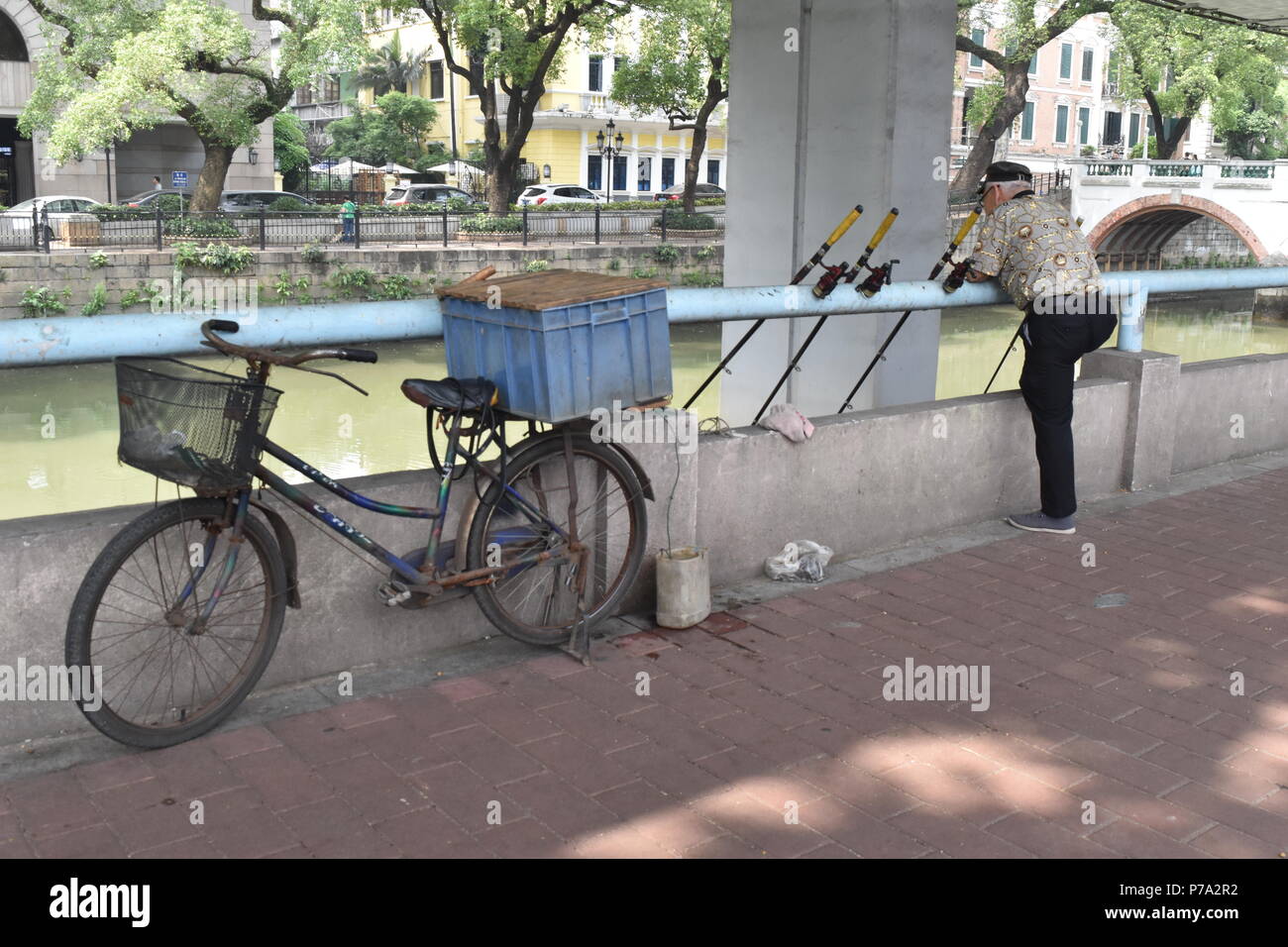 Poissons pêcheur Chinois urbains par le centre-ville de Guangzhou et canal vieux vélo Banque D'Images