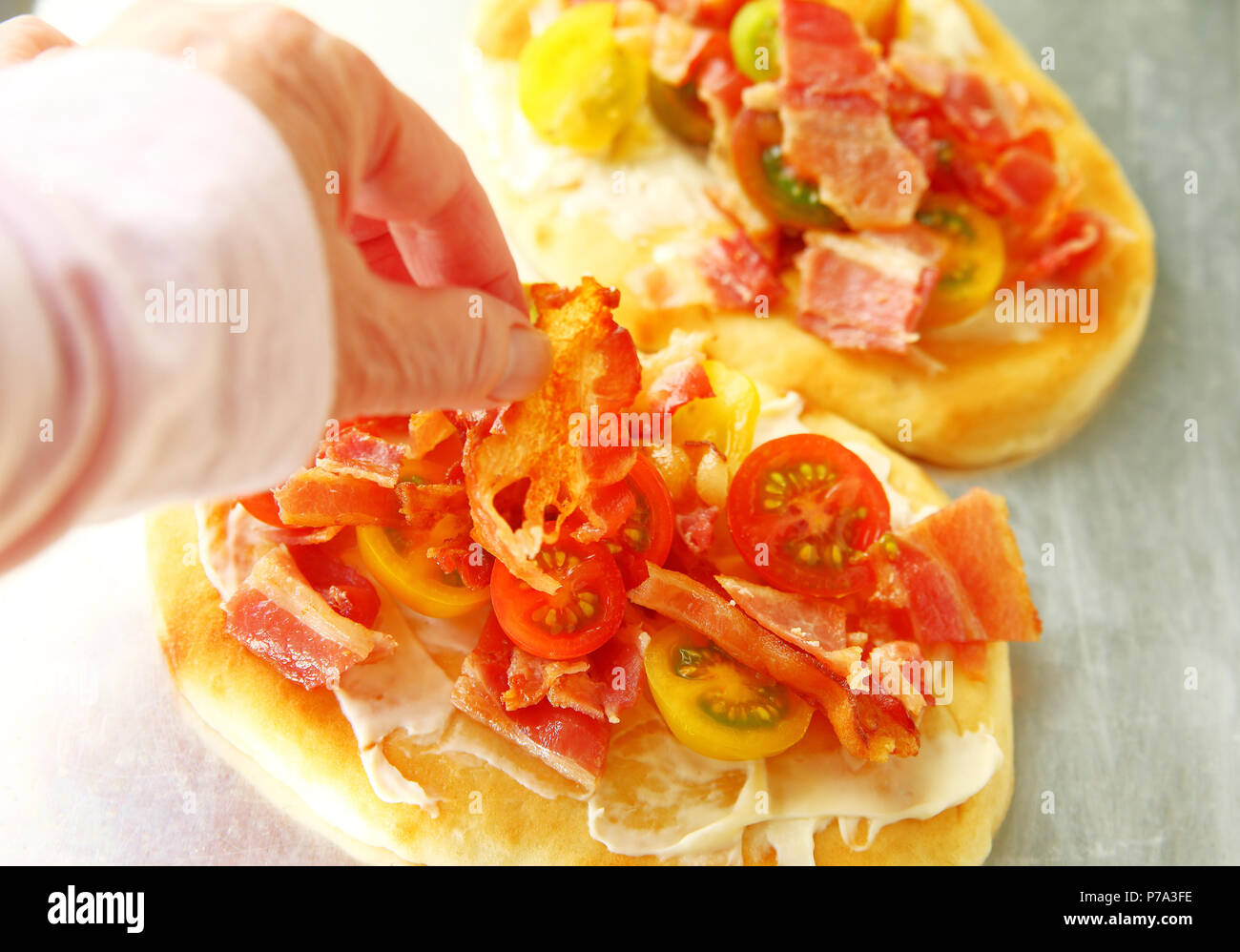 Une femme met un morceau de bacon sur pizzas naan avec tomates cerises Banque D'Images