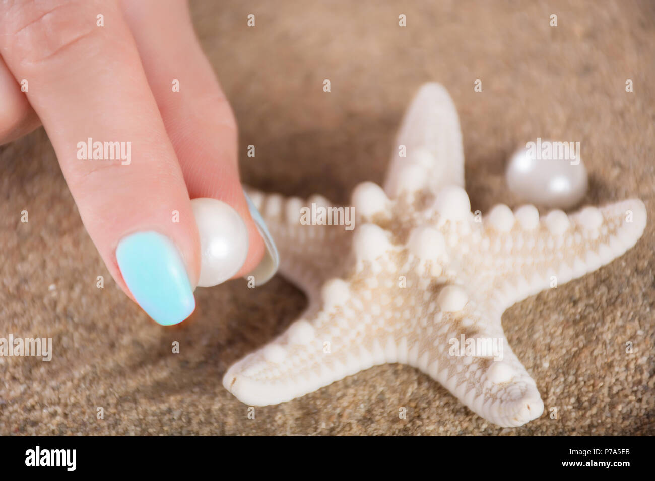 Jeune fille doucement les doigts avec des ongles manucure bleu pearl  holding polonaise et des étoiles de mer sur plage sable floue en  arrière-plan. Concept de vacances d'été Photo Stock - Alamy