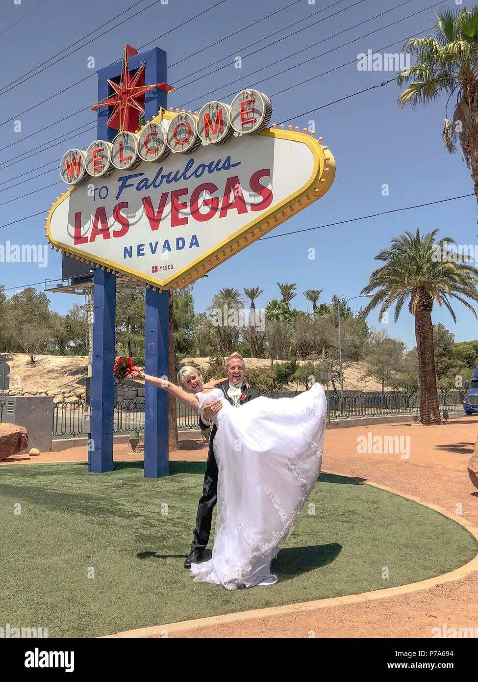 Mariée et marié à Bienvenue au Fabuleux panneau de Las Vegas. Un couple de nouveau-né pose pour la photo, le pot-de-vin soulevant la mariée avec le bouquet dans ses bras. Banque D'Images