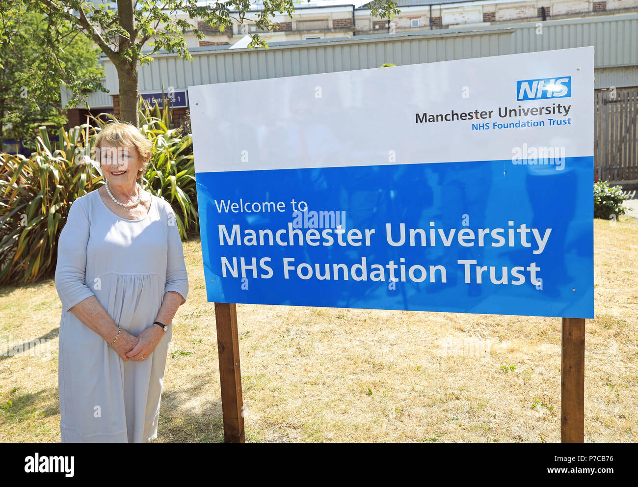 Juin Rosen, se tient à côté d'un signe de la Manchester University NHS Foundation Trust à Trafford General Hospital de Manchester, pour marquer le 70e anniversaire de la NHS. Banque D'Images