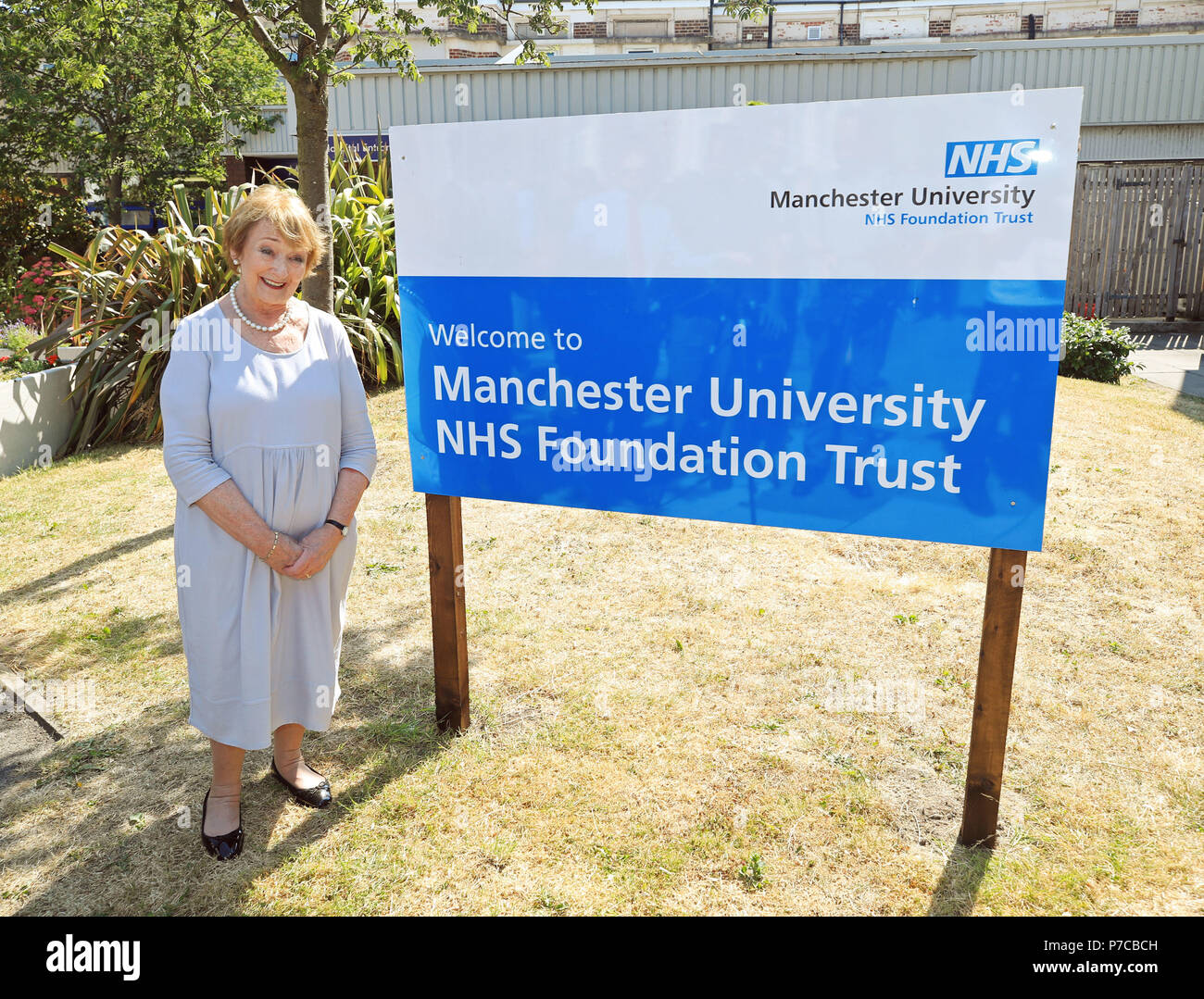 Juin Rosen, se tient à côté d'un signe de la Manchester University NHS Foundation Trust à Trafford General Hospital de Manchester, pour marquer le 70e anniversaire de la NHS. Banque D'Images