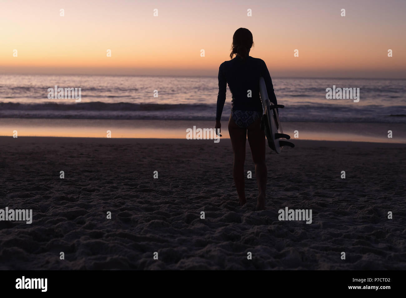 Fit woman holding surfboard in la plage au crépuscule Banque D'Images
