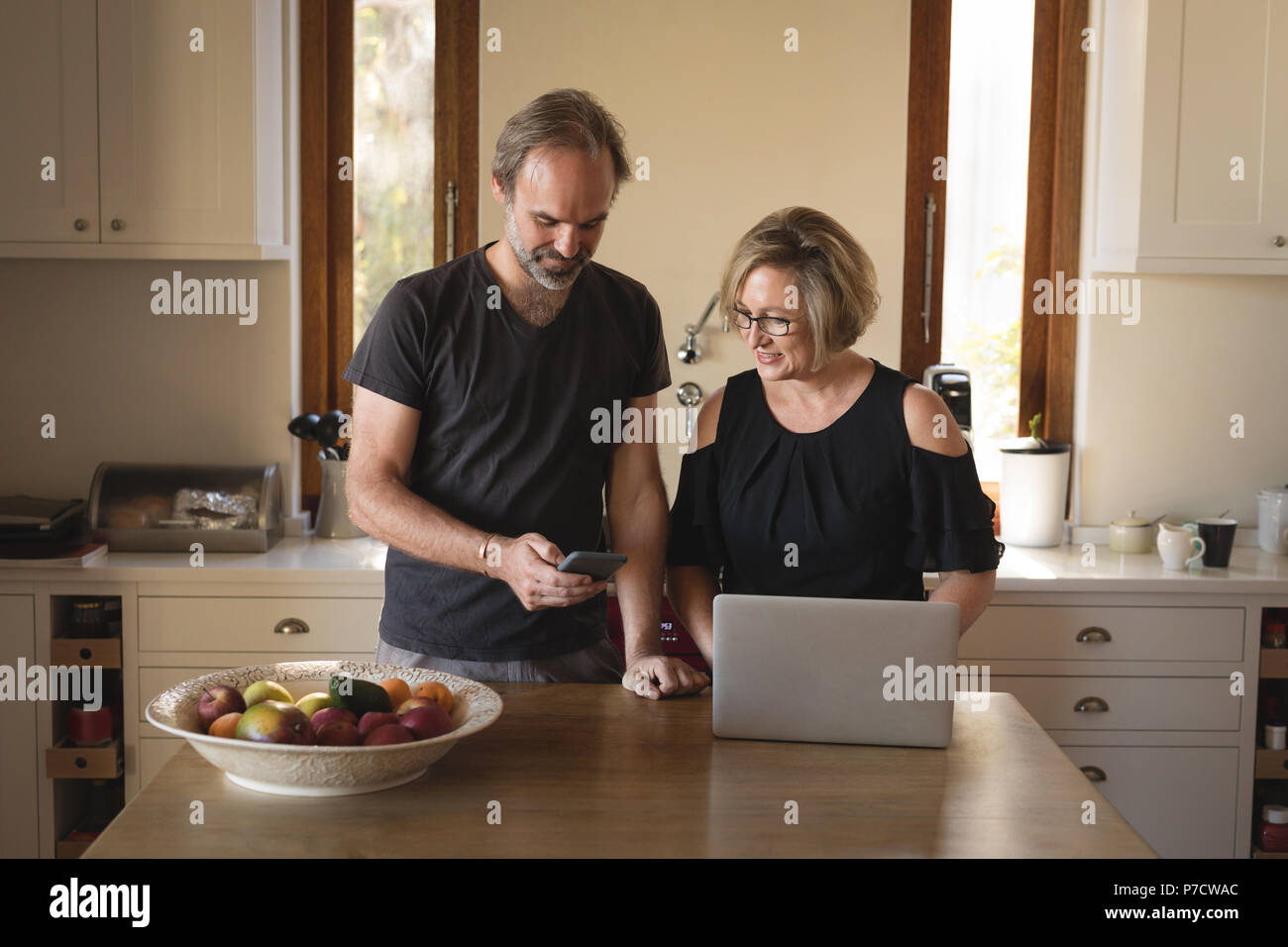 Couple using mobile phone and laptop in kitchen Banque D'Images