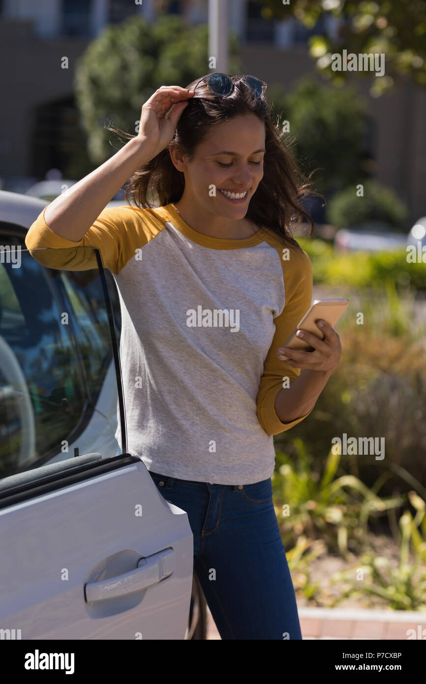 Woman using mobile phone debout près de la voiture électrique Banque D'Images