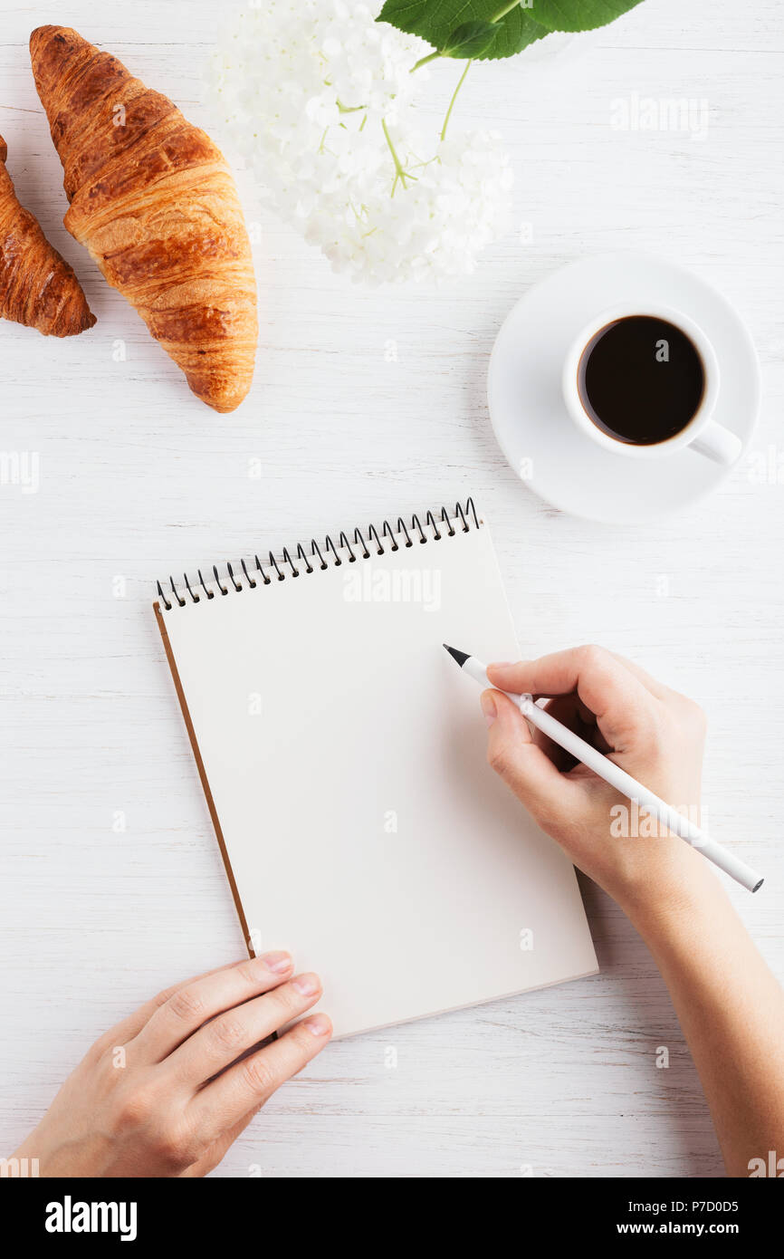 Woman's hand writing in notebook sur table en bois blanc. Lieu de travail et de planification, conception, temps matin vue du dessus. Banque D'Images