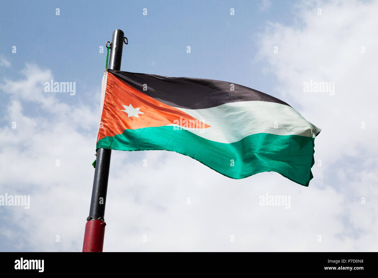 Brandissant le drapeau de la Jordanie sur le vent sur nuageux ciel bleu Banque D'Images