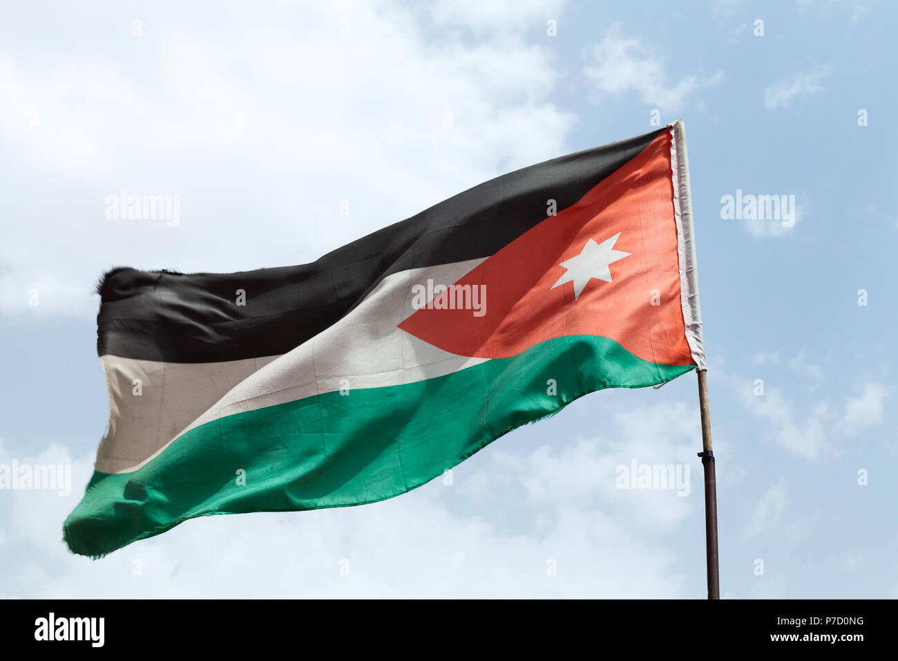 Brandissant le drapeau de la Jordanie sur le vent sur nuageux ciel bleu dans une journée ensoleillée Banque D'Images