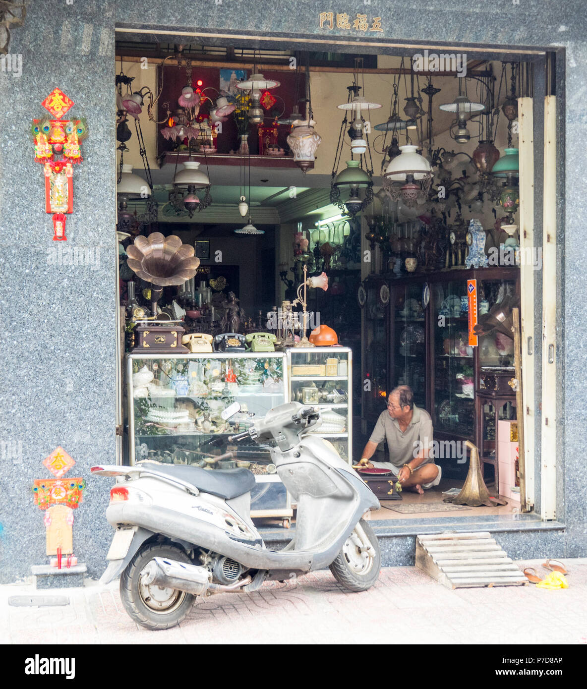 Un homme assis et de manger le déjeuner à l'entrée de sa boutique d'antiquités dans Lê Công Kiều Street, Antique Street, Ho Chi Minh City, Vietnam. Banque D'Images