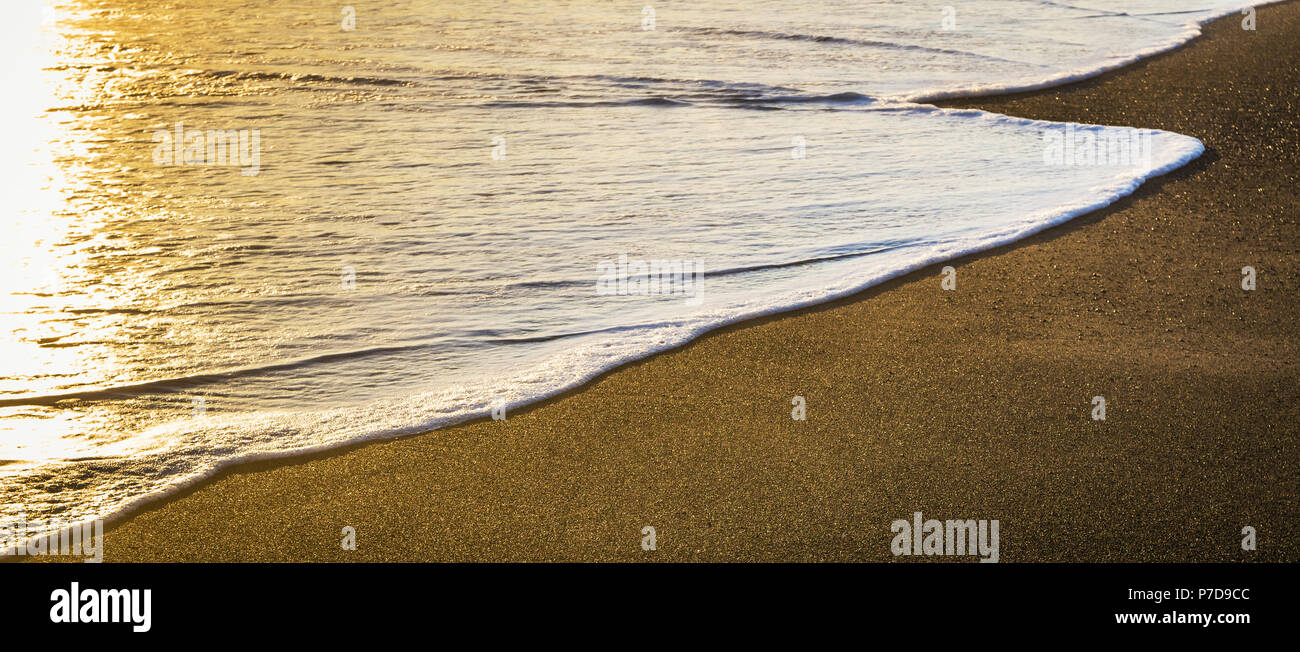 Coucher de soleil sur la plage avec la fin d'un océan vagues écumeuses récupérer le sable. Papier peint et toile avec copie grand espace. Banque D'Images