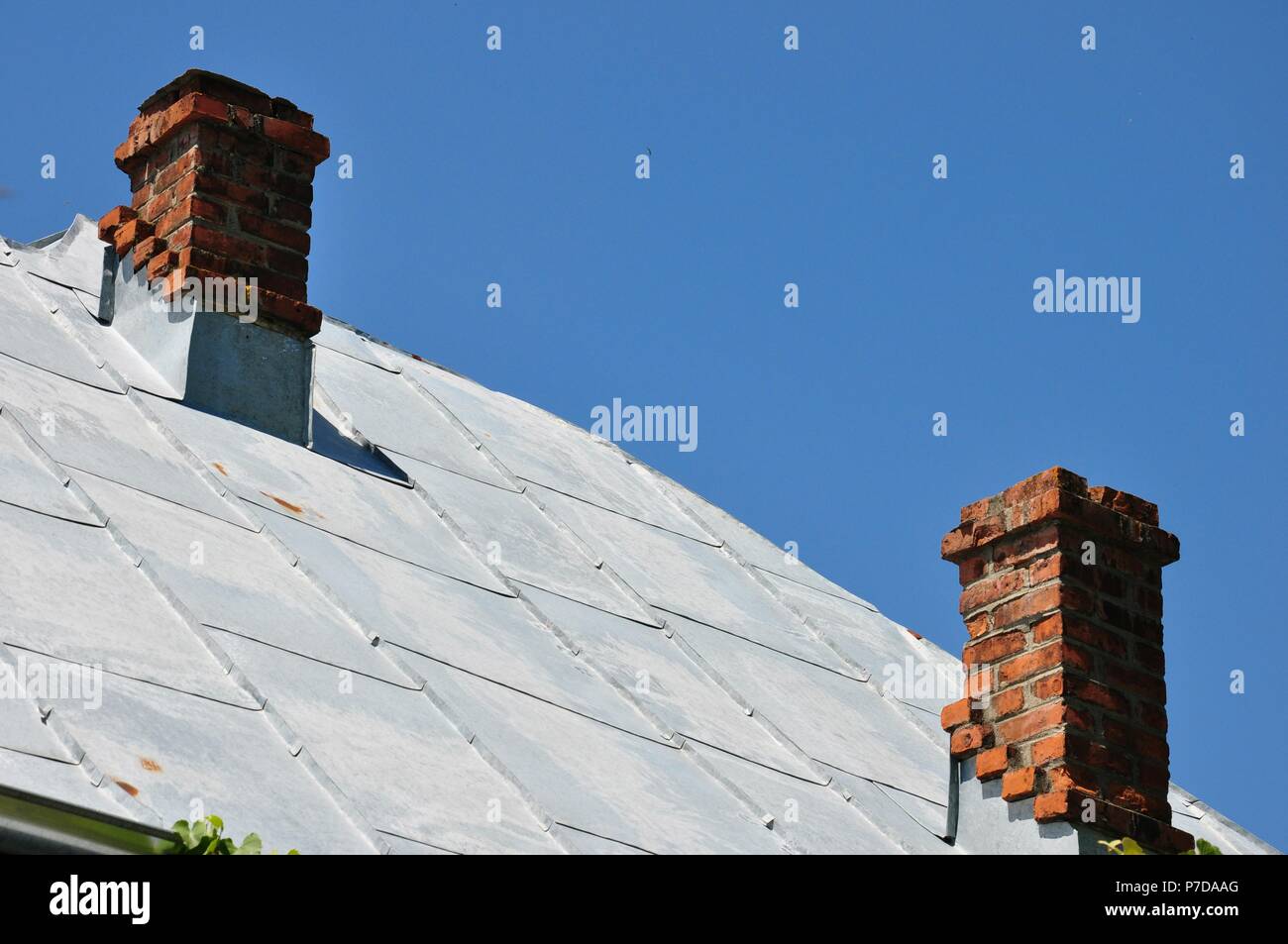 Toit en métal gris feuille avec deux cheminées traditionnelles faites de briques sur une maison dans la campagne, avec un fond de ciel bleu clair, copy space Banque D'Images