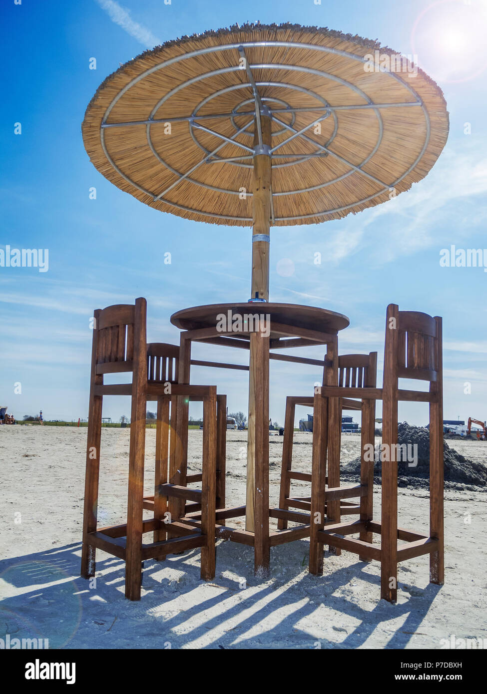 Vue profonde sur une plage, table avec quatre tabourets et reed parasol sur la plage avec des reflets de l'objectif de ciel bleu avec nuages voile. Banque D'Images