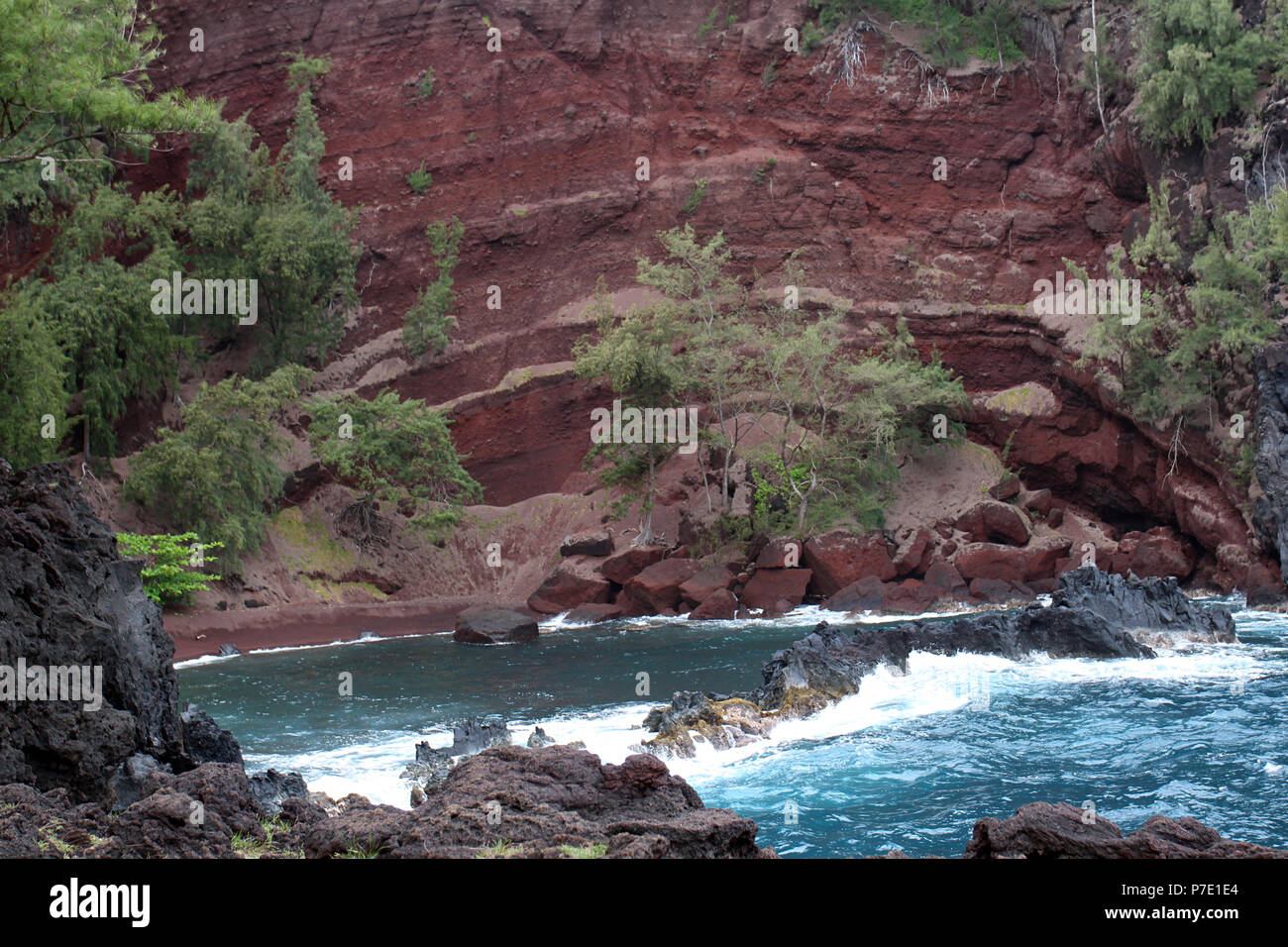 D'imposants, transparente, falaises rouges menant à une anse de la plage de sable rouge sur Kaihalulu Bay, avec des vagues de l'océan Pacifique s'écraser dans la pierre de lave je Banque D'Images