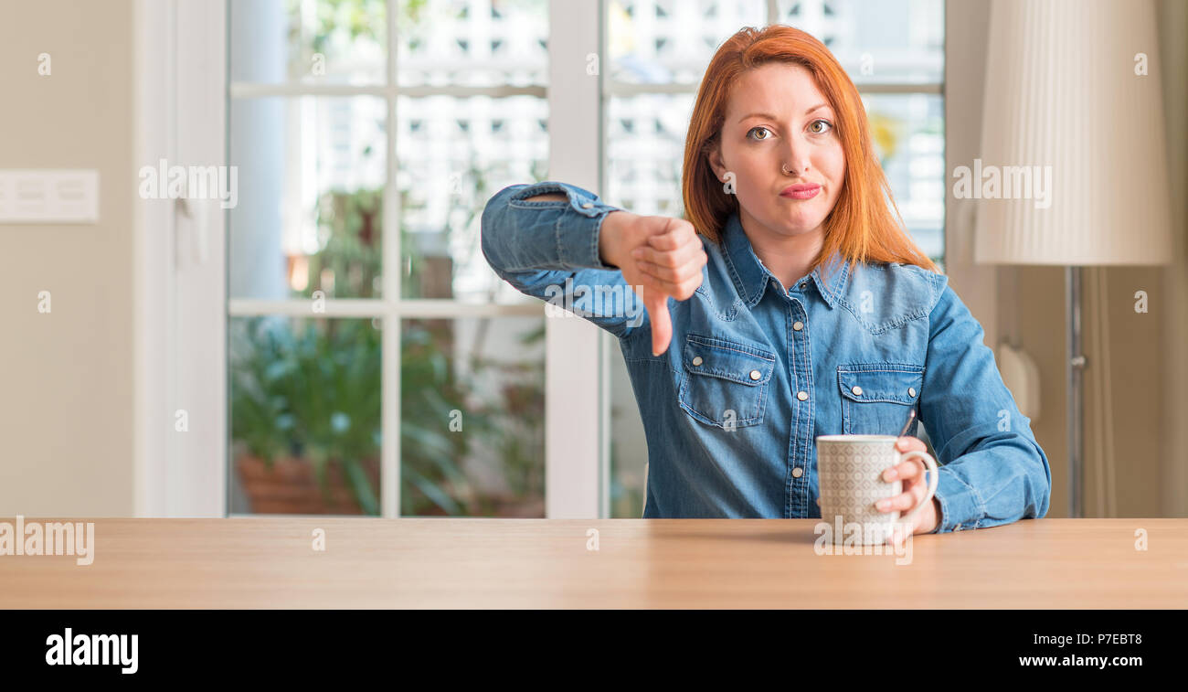 Rousse femme tenant une tasse de café avec visage en colère, signe négatif montrant non avec vers le bas, le rejet de la notion Banque D'Images