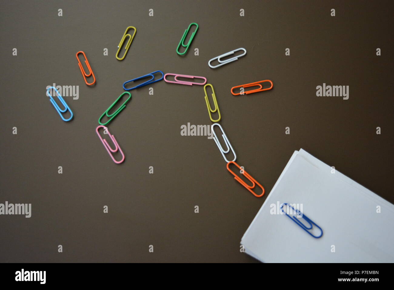 Du papier de couleur disposés avec les clips d'un point d'interrogation et avec des feuilles de papier blanc pour l'enregistrement sur un fond mat brun. Banque D'Images