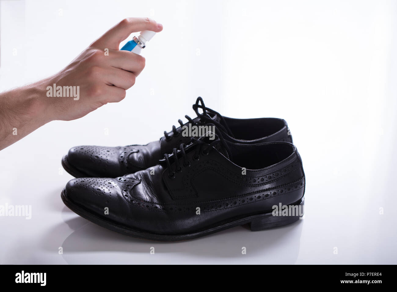 La main de l'homme déodorant propagation sur les chaussures malodorantes contre fond blanc Banque D'Images