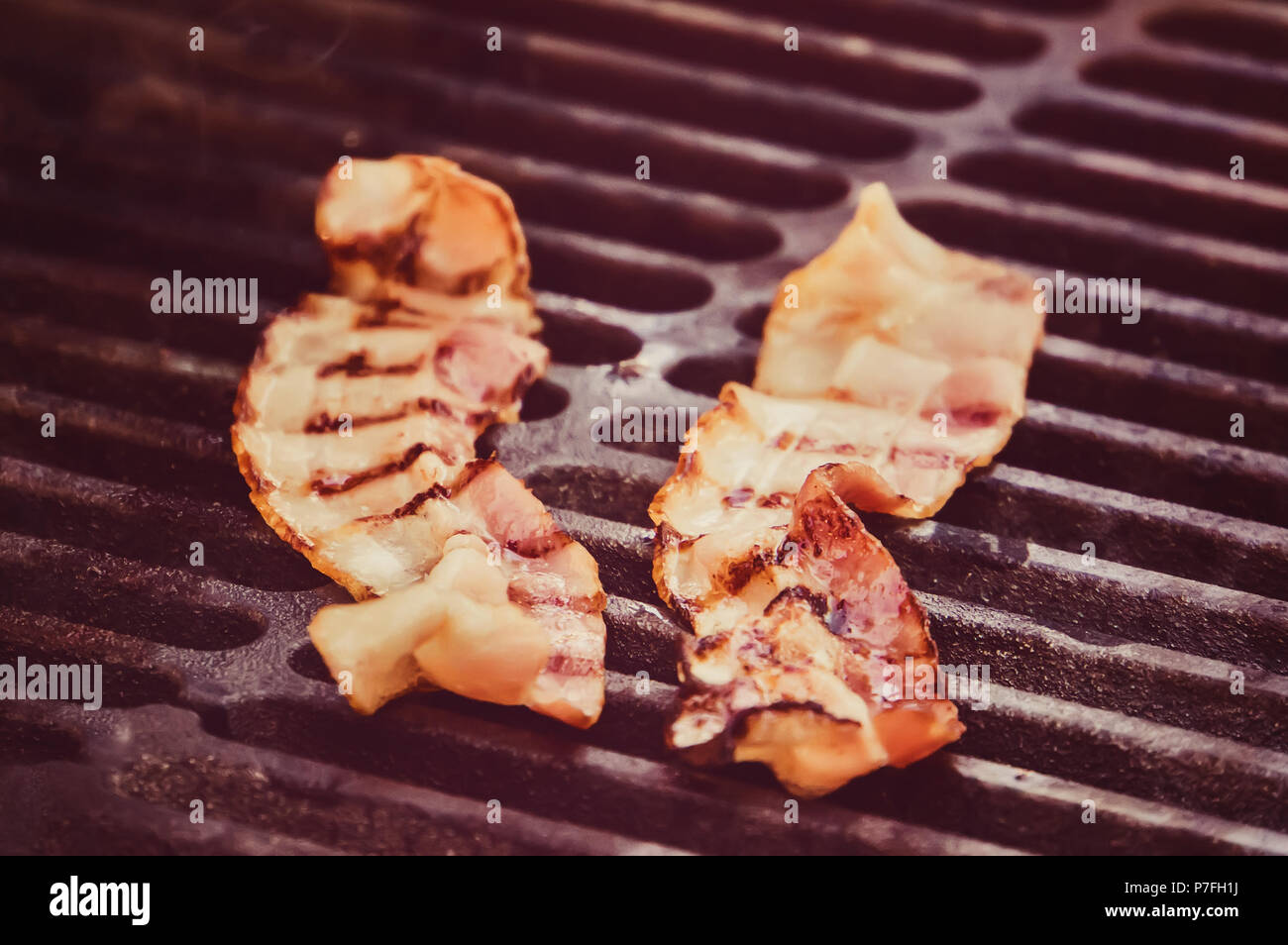 Tongs holding crispy bacon fumé barbecue grillé, cuit en tranches sur la fumée de Barbecue grill, Close up. bandes sur les tranches de bacon. Les ingrédients pour la sa Banque D'Images